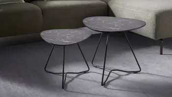 Zwei schwarze Beistelltische vor grünem Sofa.