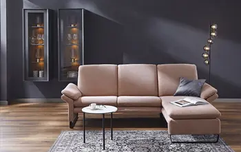 Rosa Ecksofa mit schwarzen Kufen und dicken Rückenkissen, dekoriert mit einem blauen Kissen und aufgeschlagenen Buch.