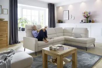 Eine Frau sitzt entspannt auf einem weißen Ecksofa mit klappbaren Kopflehnen.