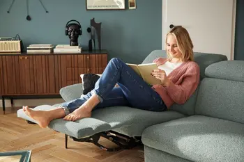 Frau sitzt auf einem grünen Sofa, mit ausgeklappter Fußlehne.