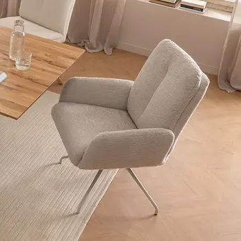 Armlehnstuhl mit beigem Stoff und beigem Metallgestellt neben Holztisch in einem hellen Esszimmer. 