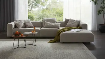 Hellgraues Ecksofa in elegantem Wohnzimmer mit beigem Teppich und großem Fenster.