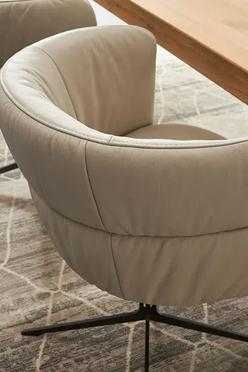 Seitenansicht eines beigen Esszimmerstuhls mit Lederbezug und abgerundeter Rückenlehne.