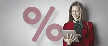 Frau mit rotem Oberteil und Brille hält ein Tablet, im Hintergrund ein großes Prozentzeichen auf grauer Wand.
