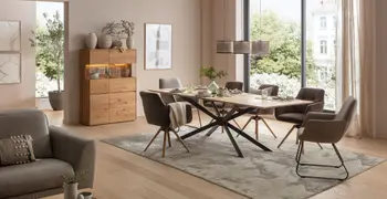 Großer Esstisch aus Massivholz mit Armlehnstühlen in grau in einem hellen Esszimmer mit Blick ins Grüne.