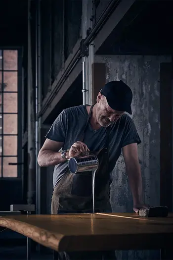 Mann bei der Herstellung eines Design Esstisches aus Massivholz, der mit Epoxidharz in Lücken gefüllt wird.