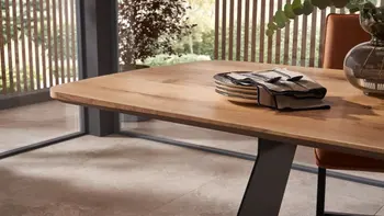 Massivholz Esstisch mit abgerundeter Tischplatte, auf der Geschirr gestapelt ist und Besteck oben darauf liegt.