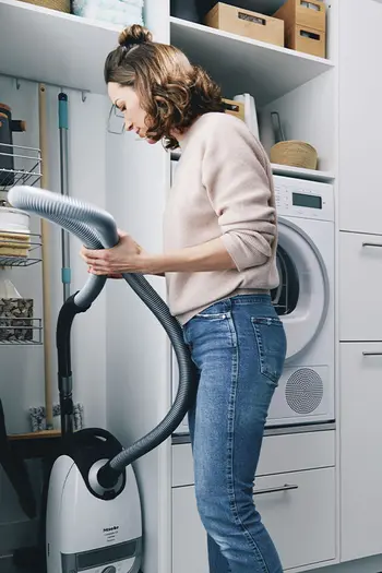 Frau verstaut Staubsauger im Hauswirtschaftsschrank