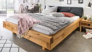 Massivholzbett mit Holzmaserung und einem Kopfteil aus schwarzem Leder in einem gemütlichen Schlafzimme rmit Sessel und passendem Massivholz Couchtisch.