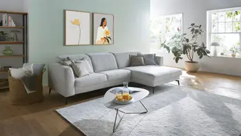 Helles Wohnzimmer mit hellem Ecksofa und ovalem Beistelltisch. 