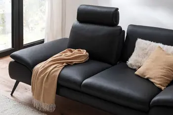 Schwarzes 3-Sitzer Ledersofa mit aufgestellter Kopfstütze und einer Decke und Kissen auf der Sitzfläche.