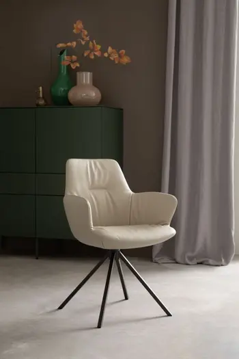 Designer Polsterstuhl mit schwarzem Fußgestell und Leder bezogen in Sand in einem hellen Zimmer, hinter dem Stuhl steht ein modernes grünes Highboard auf dem Blumenvasen stehen.