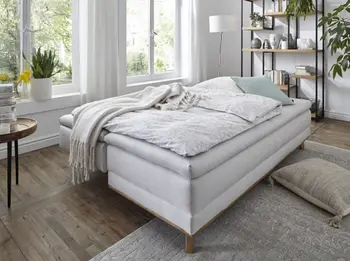Bild eines weißen Sofas, das umgebaut ist zum Bett und mit weißen Decken und Kissen und grünem Kissen dekoriert ist.