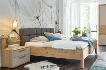 Bett mit Holzrahmen und grau gestepptem Kopfteil neben einem Nachttisch aus Holz mit beigen Fronten.