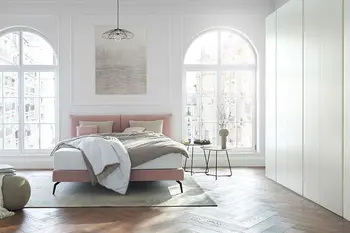 Altbauwohnung mit hohen Decken und großen Fenstern in dem ein rosa Design Polsterbett steht.