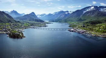 Atemberaubende Luftaufnahme von Sykkylven, Norwegen – die Heimat der Marke Svane®. Die beeindruckende Landschaft mit fjordähnlichen Gewässern, einer Brücke und schneebedeckten Bergen verkörpert die natürliche Schönheit und Ruhe der Region.