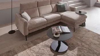 Runder schwarzer höhenverstellbarer Couchtisch vor einem beigen Ecksofa.