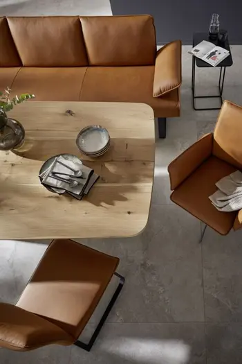 Moderne Sitzbank mit Armlehne, Freischwinger und Armlehnstuhl in cognacfarbenem Leder an einem Esstisch aus Holz von oben.