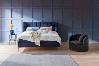 Gemütliches Schlafzimmer mit blauer Wand, blauem Polsterbett und weißer Bettwäsche.
