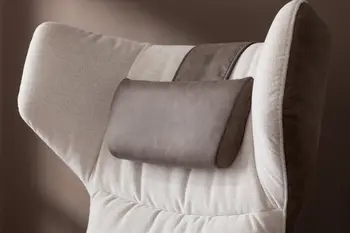 Kopfteil eines Ohrensessels in beige, an dem ein braunes Kissen über die Rückenlehne hängt, der Sessel ist außen mit braunem Stoff bezogen.