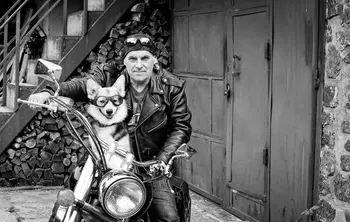 Schwarz-weiß Aufnahme eines Motorradfahrers, der mit einem Hund mit Schutzbrille auf einem Motorrad sitz.