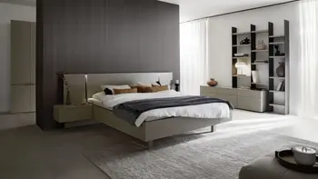 Modernes Schlafzimmer mit einem grauen Bett, an dem zwei hängende Nachtkonsolen befestigt sind, im Hintergrund ist ein Teil eines Schranks in der gleichen Farbe zu sehen und rechts vom Bett ein Regal, das an einem grauen Sideboard befestigt ist.