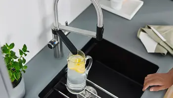 Moderne Küchenarmatur mit flexiblem Auslauf füllt eine Glaskaraffe mit Wasser und Zitronens