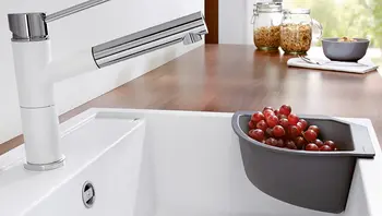 Weiße Küchenarmatur mit Edelstahlakzenten neben Spüle mit Einsatzschale, in der rote Weintrauben liegen.