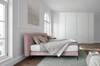 Rosa Design Polsterbett mit weißem Kleiderschrank in einer Altbauwohnung.