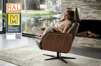 Gütesiegel "Goldene M" auf einem Bild eines Relaxsessel, der an der Armlehne außen mit Holz verkleidet sind ist und innen mit Leder, auf dem Sessel sitzt eine Frau und liest entspannt.