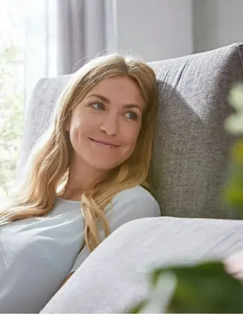 Blonde Frau, die auf einer grauen Couch liegt.