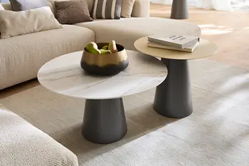 Zwei runde Couchtische vor einem beigen Ecksofa, mit schwarzem Fuß und weißer oder gelber Tischplatte.