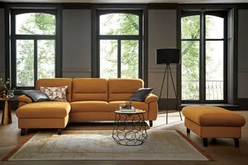 Gelbes Ecksofa mit passendem gelben Hocker in einem Zimmer mit bodentiefen Fenstern.