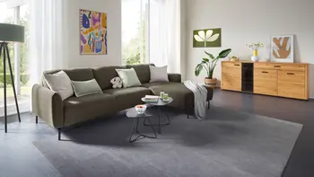 Helles Wohnzimmer mit Ecksofa aus grünem Stoff und einer Kommode.