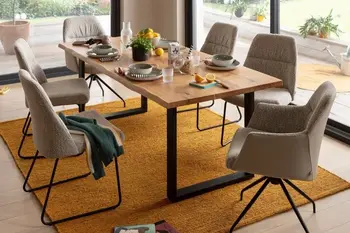 Moderner Massivholz Esstisch mit schwarzen Kufen in einem hellen Raum, um den Tisch stehen mehrere graue Stühle mit und ohne Armlehne.