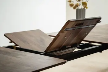 Dunkelbrauner Esstisch, bei dem die Tischplatten Erweiterung gerade ausgeklappt wird.