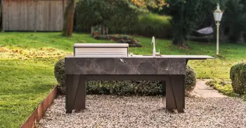 Dunkle Outdoorkueche von OCQ im Kiesbett eines Gartens.