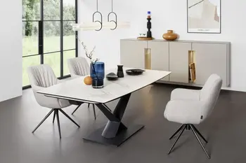 Drei bequem gepolsterte beige Armlehnstühle, die eine moderne Faltenbildung an der Rückenlehne haben und ein schwarzes Metallgestell und um einen modernen Keramik Esstisch in einem hellen Raum stehen.