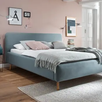 Ein mit einer blauen Decke bedecktes Bett mit Kissen und Polstern in einem Schlafzimmer im Innenbereich mit einem Nachttisch in der Nähe.