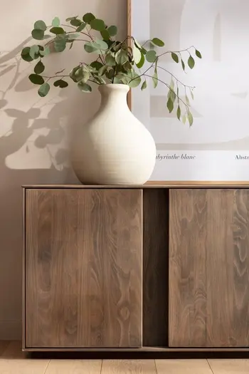 Modernes Sideboard aus geschroppter massiver Buche mit zwei Türen, auf dem eine große weiße Vase mit Blumen steht.