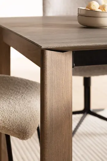 Bein und teil der Tischplatte eines modernen Esstisches aus massiver Buche, an dem ein heller Stuhl steht.