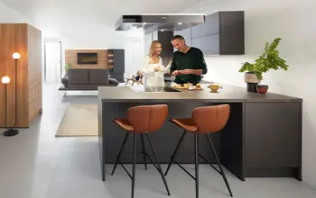Eine Frau und ein Mann stehen in einer modernen dunklen Küche mit Barhockern.