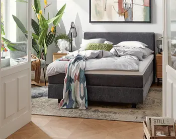 Dunkelgraues Bett in einem kleinem gemuetlichen Schlafzimmer.