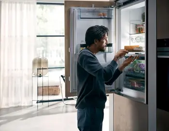 Mann steht vor dem geöffnetem Kühlschrank und nimmt etwas.
