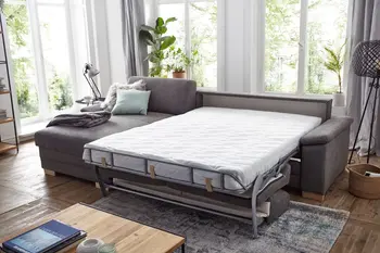 Graues Ecksofa, das zum Doppelbett umgebaut ist, dekoriert mit grauer Decke und weißem Fellkissen und grünem Kissen.