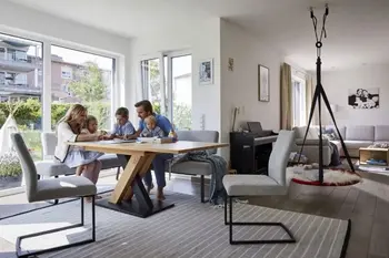 Heller Wohnbereich mit grauen Freischwinger Stühlen und einer grauen Sitzbank auf der eine Familie sitzt und ein Spiel spielt.