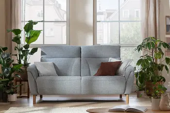 Klassisches 2-Sitzersofa in hellgrauem Stoff in Wohnzimmer mit vielen Grünpflanzen.