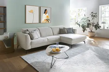 Modernes Ecksofa in hellgrauem Stoff mit passendem Couchtisch in einem hellen Wohnzimmer.