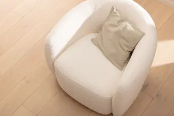 Runder Sessel mit niedriger Rückenlehnemit cremefarbenem Stoffbezug, auf dem ein beiges Kissen liegt.