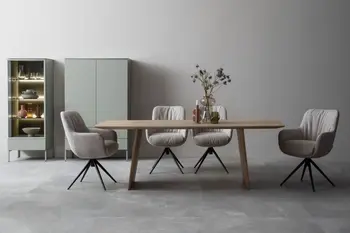 Moderner großer Esstisch aus hellem Holz in einem hellen Raum, um den vier graue Armlehnstühle mit schwarzem Gestell stehen.